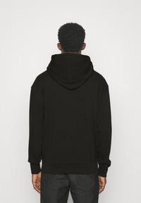 Felpa nera con tasca a marsupio e cappuccio con cordino. Tessuto morbido, maniche lunghe e polsini e orlo a coste. Design semplice e minimal.