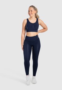 Ensemble de sport marine composé d'un soutien-gorge de sport à fermeture éclair à l'avant et de leggings taille haute, fabriqué dans un tissu lisse et extensible avec des détails de couture.