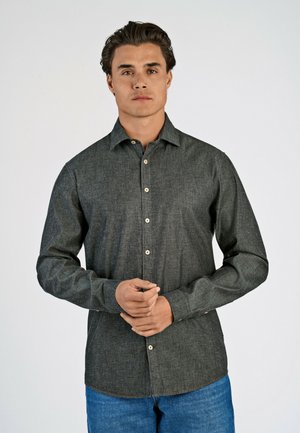 Donkergrijze button-up overhemd van een gestructureerde stof, met een standaardkraag en lichtgekleurde knopen, gecombineerd met blauwe jeans.