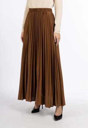Modelo con una falda plisada marrón hasta el suelo, con cintura elástica, un top de color crema y zapatos negros de tacón.