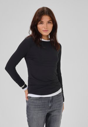 Zwarte langemouwen T-shirt met een witte kraag en manchetten, gemaakt van een gladde stof. Gecombineerd met grijze jeans die een aansluitend ontwerp hebben.