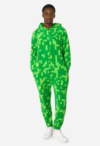 Green fleece onesie with a pixelated pattern in varying shades of green, featuring a zip front and hood, worn with white sneakers.