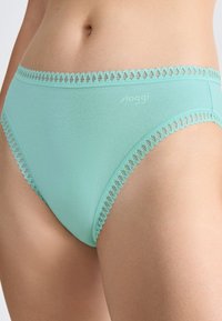 Lichtblauwe katoenen onderbroek met kantafwerking, gedragen op de onderrug van een persoon, waarbij de tailleband en het heupgebied zichtbaar zijn.