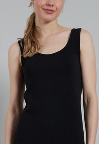 Zwarte tanktop met een ronde halslijn en brede schouderbanden, gemaakt van zachte stof met een gladde textuur. Geschikt voor casual draagstijl.