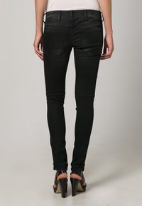 Jeans negros ajustados con una textura suave, que cuentan con bolsillos traseros y detalles de costura sutiles, combinados con zapatos de tacón negros.