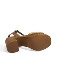 Braune Sandale mit Absatz und dicker Sohle, strukturiertem Riemen und Nietenakzenten. Verfügt über ein Ausschnitt-Design mit einem verstellbaren Knöchelriemen.