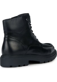 Botas de tobillo de cuero negro con puntera redondeada, diseño con cordones y suela de goma gruesa. Presenta un detalle de costura en la parte superior y una textura suave.