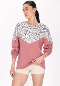Leopárdmintás pulóver, rózsaszín alsó résszel, puha anyagból, hosszú ujjakkal és kerek nyakkivágással. Elasztikus mandzsettákkal és chevron mintával rendelkezik.