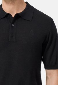 Svart polo skjorta tillverkad av mjukt material, med en knäppbar krage, korta ärmar och en diskret präglad logotyp på bröstet.