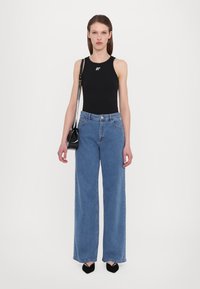 Black sleeveless top with white logo, light blue high-waisted wide-leg jeans, and black handbag. Model wearing pointed black shoes.