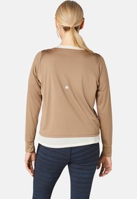 Langärmliges Shirt aus sandfarbenem Stoff mit rundem Ausschnitt, das einen subtilen weißen Punkt auf dem Rücken und einen kontrastierenden unteren Saum aufweist.