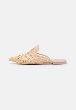 Mule de punta puntiaguda con parte superior tejida en beige claro que presenta patrones bordados intrincados. Suela plana con una plantilla rosa lisa.