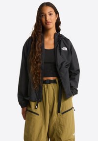 Czarna kurtka z kapturem zapinana na suwak z przodu z logo, zestawiona z luźnymi spodniami w jasnym oliwkowym kolorze z bocznymi kieszeniami i regulowanym paskiem.