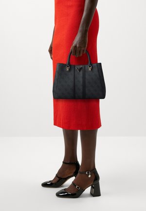 Borsa nera con materiale testurizzato, dettagli in metallo dorato e doppi manici superiori, tenuta da una persona con un vestito rosso e tacchi neri.