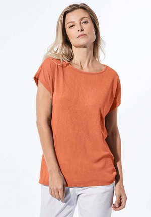 Oranges Baumwoll-T-Shirt mit kurzen Ärmeln und einem Rundhalsausschnitt, kombiniert mit weißen Hosen, vor einem hellen Hintergrund präsentiert.