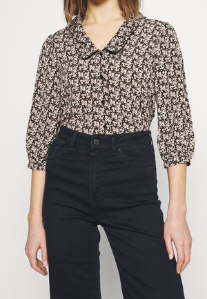 Schwarze Bluse mit einem floralen Druck in Pink, rundem Kragen und langen Puffärmeln. Kombiniert mit hochgeschnittenen dunkelblauen Jeans.