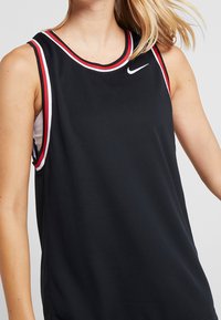 Černý sportovní tílko s texturovaným síťovaným designem a červenými a bílými detaily na límci a armholech. Zobrazené logo Nike.