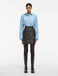 Lys blå stripete oversized skjorte med krage, kombinert med sort skinn mini skjørt og knelange svarte støvler. Jevn tekstur, skreddersydd passform.