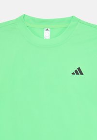 Grünes sportliches T-Shirt aus glattem Stoff. Es hat einen runden Halsausschnitt und ein kleines schwarzes Logo auf der oberen linken Seite.