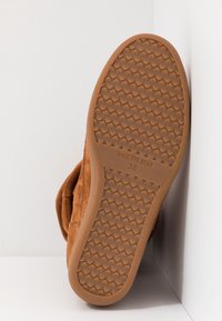 Semelle de chaussure en daim marron avec motif antidérapant en caoutchouc texturé, taille 38, avec la marque "SHOE THE BEAR" visible.