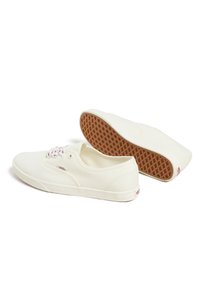 Wei�ße Leinenschuhe mit einem Low-Top-Design, gewebten Schnürsenkeln und einer Gummisohle mit Waffelmuster. Roter Logoakzent an der Seite.