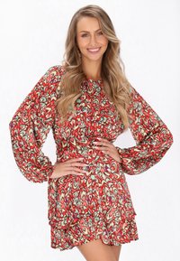Rochie roșie cu flori, cu mâneci puff, tiv volanat și un material texturat, ușor. Prezintă un model multicolor cu accente verzi și mov.