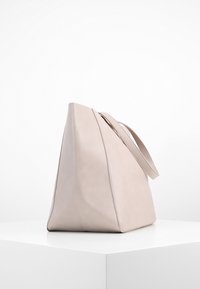 Beżowa skórzana torba na ramię o eleganckim, kanciastym kształcie, z bocznym uchwytem i gładką teksturą. Brak widocznych elementów metalowych lub wzorów.