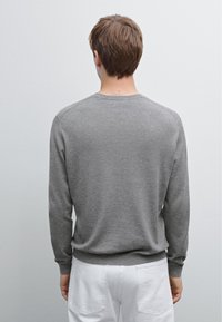 Grauer langärmeliger Pullover mit Rundhalsausschnitt, aus weichem Material, mit gerippten Bündchen und Saum, getragen über weißen Hosen.