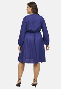 Vestido morado, de largo hasta la rodilla, con mangas largas y cintura elástica. Tejido suave con un corte holgado. Combinado con tacones negros con tiras.