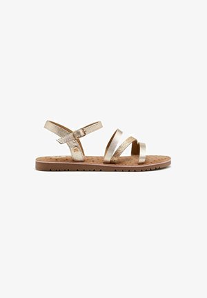 Sandal in metallo dorato con due cinturini diagonali, un cinturino alla caviglia e una suola marrone texturizzata con piccoli motivi rotondi.