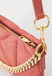 Borse a tracolla in suede rosa con un design trapuntato, hardware dorato e una tracolla a catena con chiusura a clip vicino all'apertura con zip.