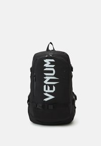 Sac à dos noir avec un grand logo "VENUM" blanc. Comprend plusieurs compartiments, des zips et des bretelles ajustables. Fabriqué en tissu durable.