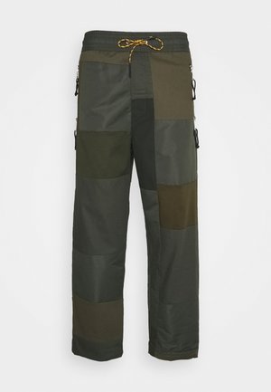 Pantalon cargo style patchwork dans différentes nuances de vert foncé avec taille élastique et cordon jaune.