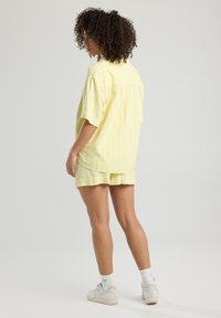 Camicetta a maniche corte a righe gialle e pantaloni abbinati realizzati in tessuto leggero. La vestibilità rilassata presenta uno yoke posteriore e spacchi laterali.