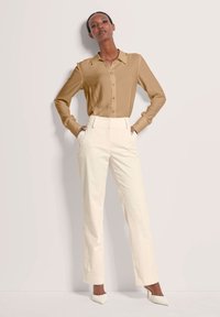 Lichtbruin overhemd met lange mouwen en knopen, gecombineerd met crèmekleurige, hooggetailleerde broek met verticale strepen en puntige witte hakken. Glad stoftextuur.