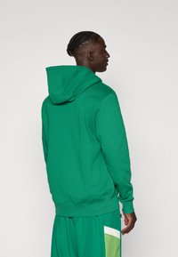 Grøn hoodie med strammet snit og stor h�ætte. Lavet af et blødt stof, med ribbede manchetter og kant, uden synlige mønstre eller hardware.