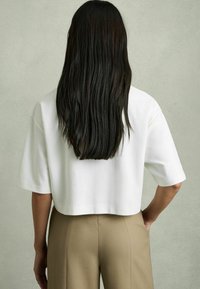 Hvid cropped skjorte med korte ærmer, glat tekstur, parret med beige skræddersyede bukser med en strømlinet pasform og bagsøm detaljer.