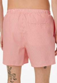 Shorts de bain rayés rouges et blancs en tissu léger, dotés d'une taille élastique et d'une poche arrière unique.