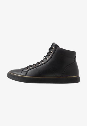 Zapatilla deportiva negra de caña alta con cuero texturizado, ojales dorados y una delgada franja dorada sobre la suela de goma negra, mostrada de perfil.