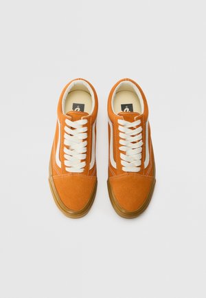 Een paar oranje suède vetersneakers met witte zijstrepen en natuurrubberen zolen op een witte achtergrond.