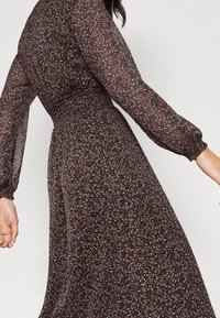 Blumenkleid aus dunklem Stoff mit langen Ärmeln. Es hat eine taillierte Taille und einen schwingenden Rock, verziert mit kleinen rosa und blauen Blumen.