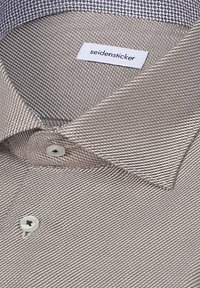Gros plan d'une chemise beige à motifs avec des boutons blancs et une étiquette de col indiquant "seidensticker."