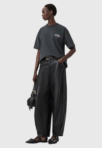 Musta ylipitkä t-paita, jossa logo rinnassa, yhdistettynä mustiin korkeavyötäröisiin leveälahkeisiin nahkahousuihin ja mustiin kullanvärisillä yksityiskohdilla varustettuihin tasapohjaisiin kenkiin.