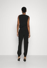 Top noir sans manches avec une taille ajustée, associé à un pantalon cargo noir ample doté de poches latérales et de poignets élastiques à la cheville.