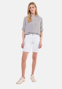Chemise rayée à col gris et blanc, associée à un short en denim blanc. Le modèle porte des baskets légères, mettant en valeur une tenue d'été décontractée.