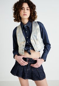 Denim outfit featuring a metallic silver vest, dark blue denim shirt, and a pleated dark blue denim skirt with colorful button accents.