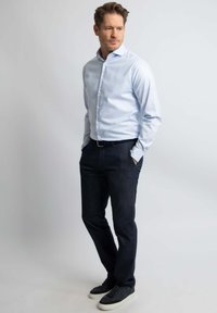 Lichtblauw overhemd met lange mouwen, gecombineerd met donkerdenim broek en zwarte sneakers. Glad textuur en getailleerde pasvorm.