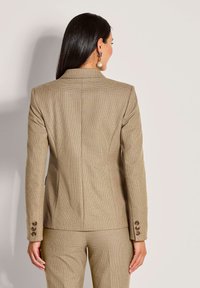 Beige op maat gemaakte blazer met een gestructureerde stof, enkele split en manchetten met drie knopen. De achterkant heeft een strak, gestructureerd ontwerp.