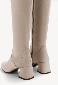 Bottes beiges au-dessus du genou en suède doux, dotées d'un talon bloc, d'une fermeture éclair sur le côté et d'un design lisse et sans couture.