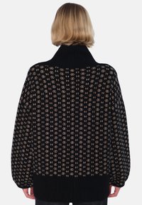 Svart mönstrad tröja med hög krage, ribbade muddar och mjuk textur, med ett mönster av ljusbruna motiv över hela plagget.